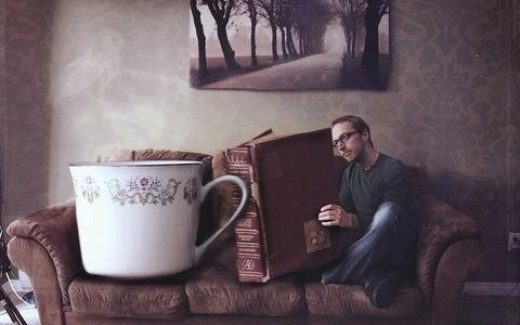 одинокий мужчина с книгой и чашкой на диване